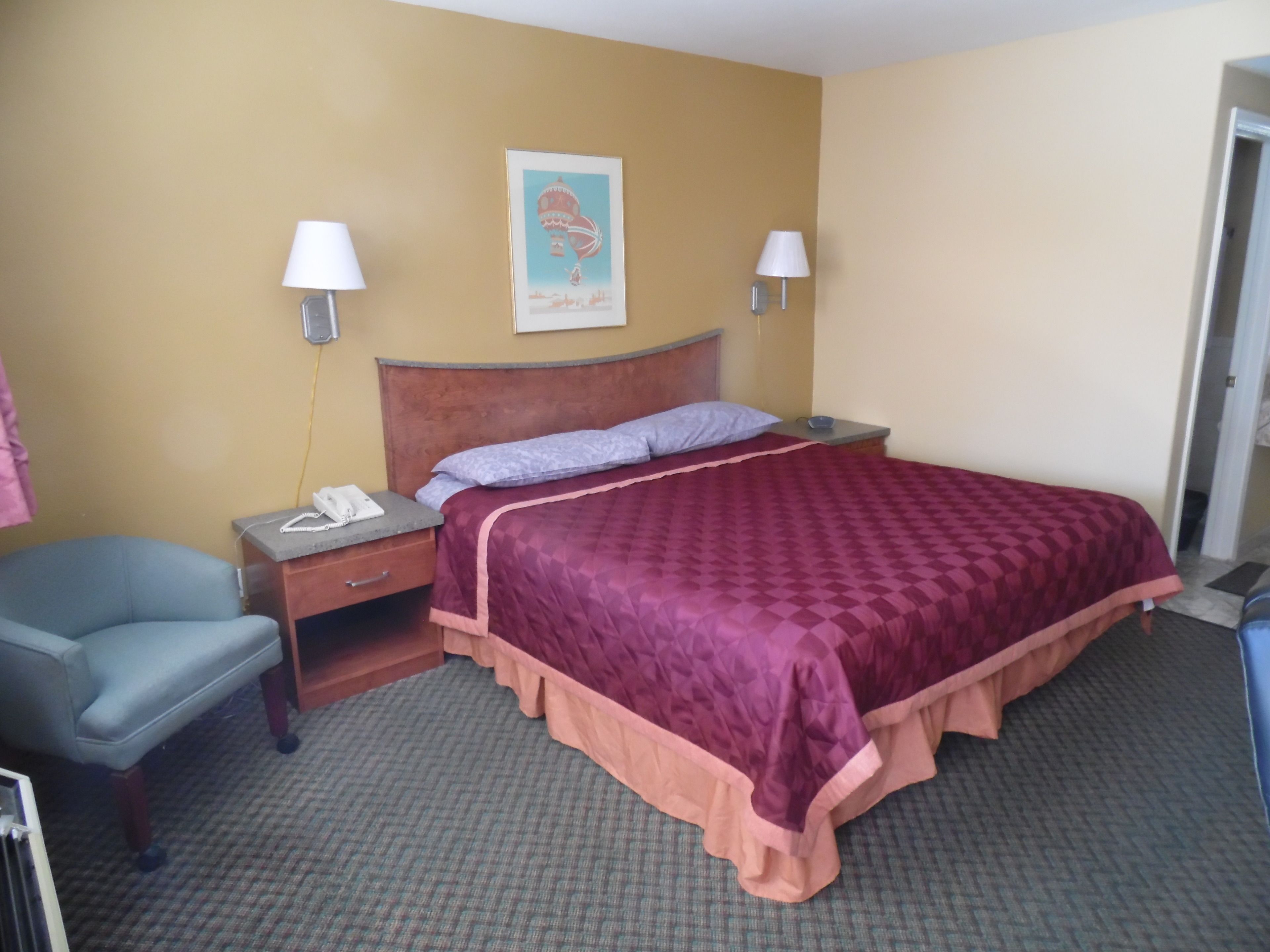 Una habitación de hotel con una cama, una silla, una mesita de noche y una lámpara fijada a la pared.