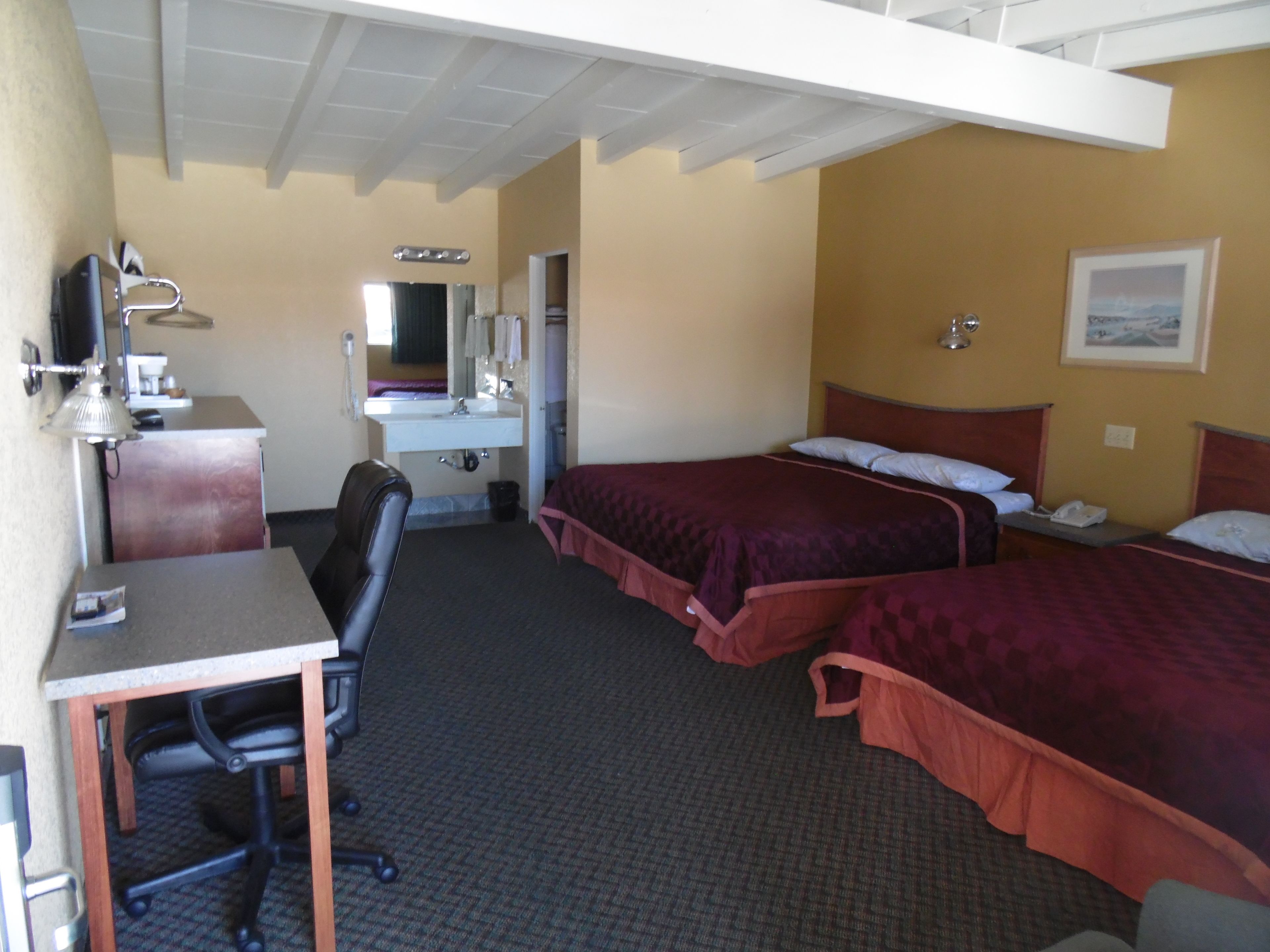 A hotel room with a desk, two beds, a mirror, a sink, and a chair.