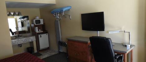 A hotel room with a bed, a desk with a chair, a television, a microwave, a small refrigerator, and a mirror.