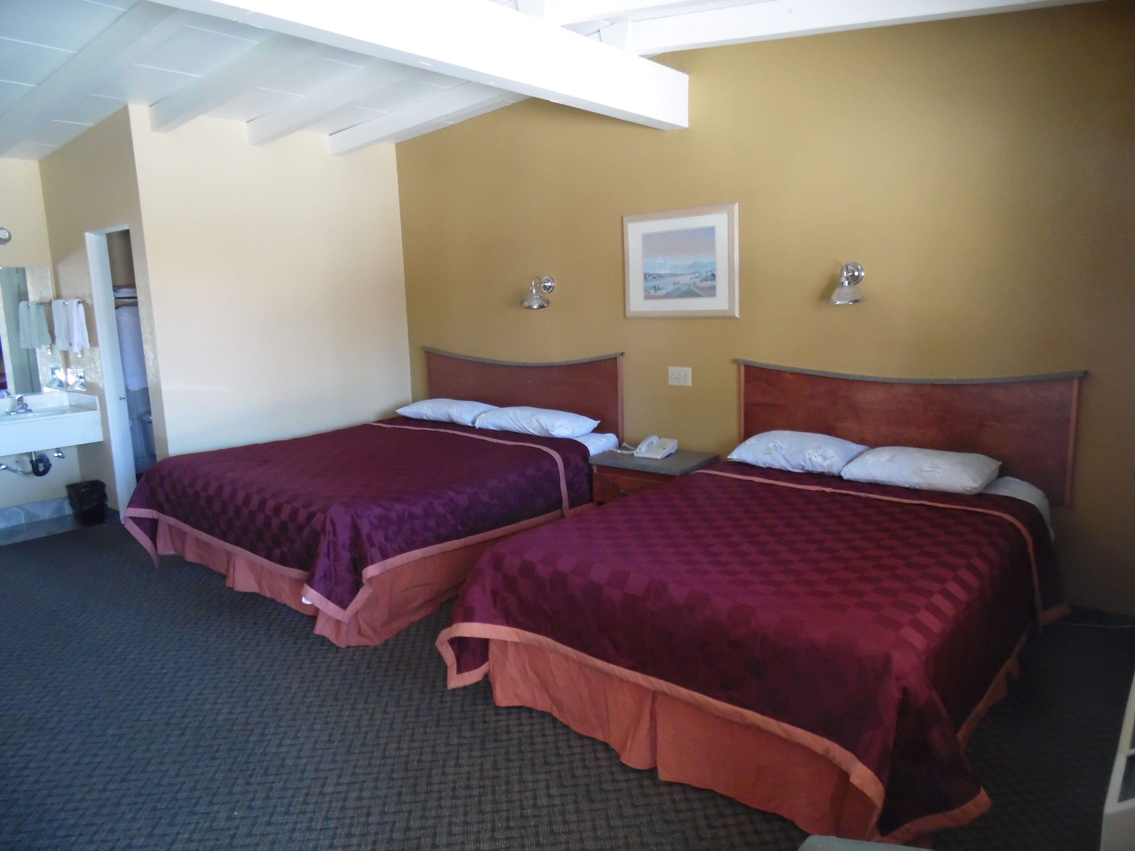 A hotel room with two beds, a bathroom with a sink, and a framed picture on the wall.