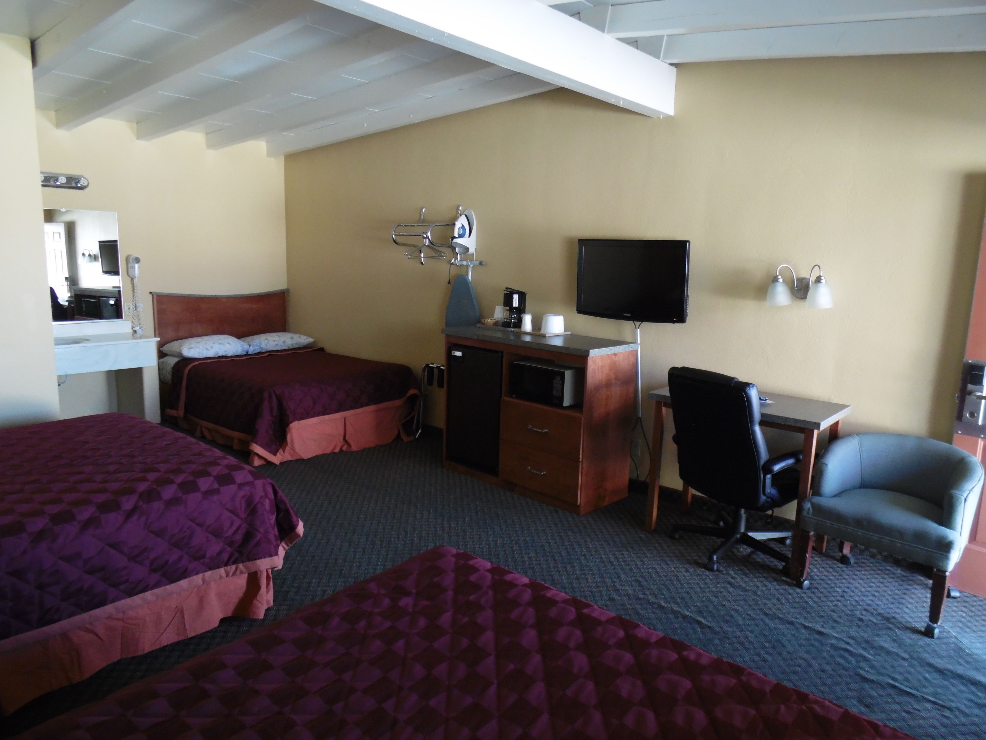 Habitación de hotel con dos camas, un escritorio con computadora, una silla, un televisor y una kitchenette pequeña.
