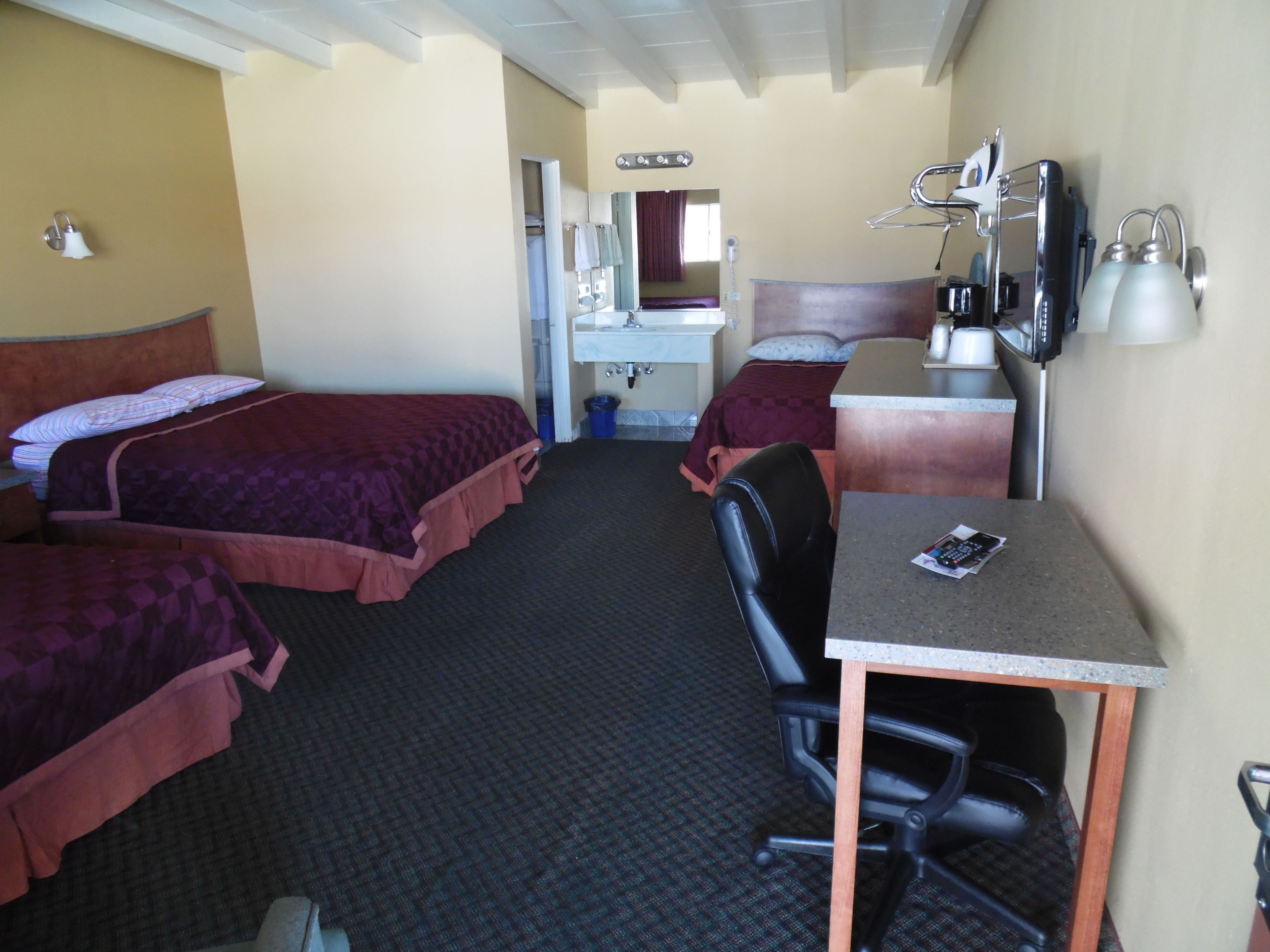 A hotel room with two beds, a desk, a chair, a sink, and a mirror.