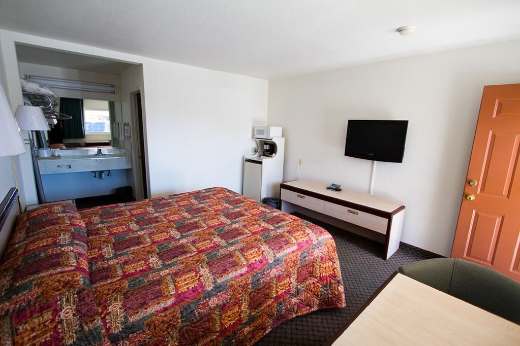 A hotel room with a bed, a desk, a television, a mirror, and a door.
