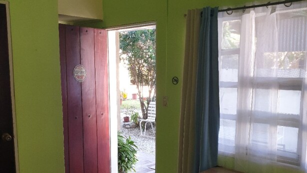Una habitación con cama, ventana con cortinas, puerta y vista al exterior.