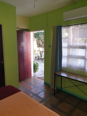 A room with a bed, a window with curtains, a door, and a view of the outside.