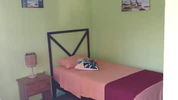 Un dormitorio con una cama individual, una mesita de noche, un ventilador de techo y dos obras de arte en la pared.