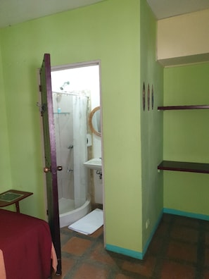 A bathroom with a shower, a sink, and a toilet. There is a door leading to another room.