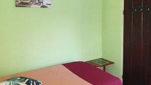 Una habitación con una cama, una mesita, una silla, una puerta y un cuadro en la pared.