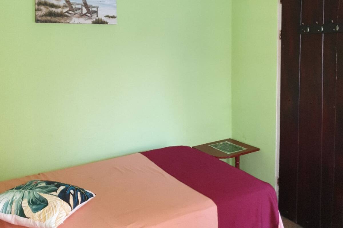 A room with a bed, a small table, a chair, a door, and a painting on the wall.
