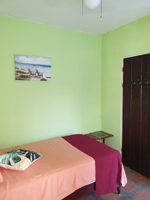 A room with a bed, a small table, a chair, a door, and a painting on the wall.