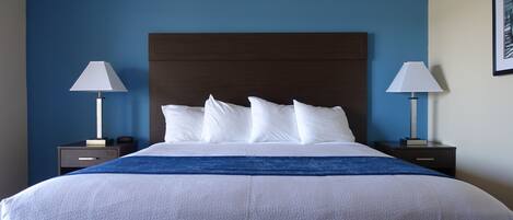 Een netjes opgemaakt bed met witte lakens en een blauw accent, met aan weerszijden twee nachtkastjes met lampen, in een kamer met blauwe wanden en een houten hoofdbord.