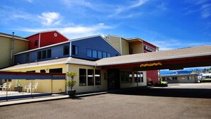 Monikerroksinen rakennus, jossa on huoltoaseman kyltti, aidattu ulkoalue istuimineen ja kirkkaan sininen taivas.