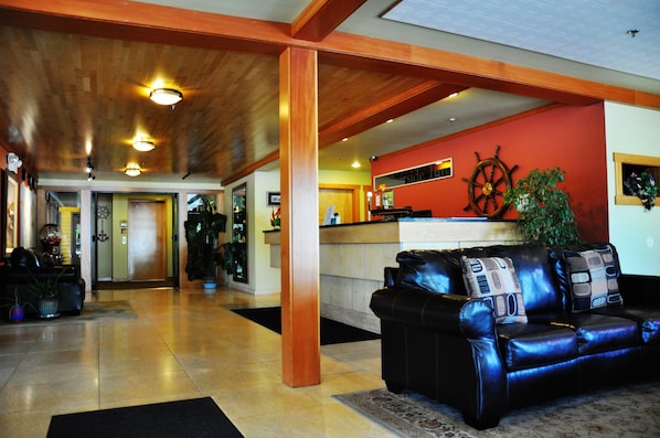 A lobby with a leather sofa, wooden beams, a ship's wheel, and a reception desk. - Harborside Inn (Port Townsend)
