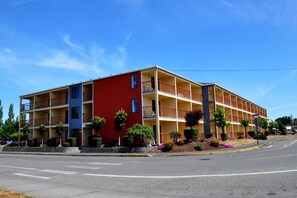 A multi-story hotel with balconies, a red and yellow facade, and landscaped gardens.