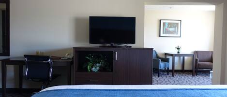 A hotel room with a bed, a television on a cabinet, a desk with a chair, and a small table with a plant.