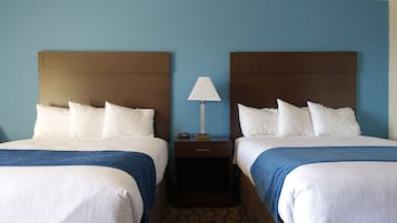 A hotel room with two beds, a nightstand with a lamp, and a patterned carpet.