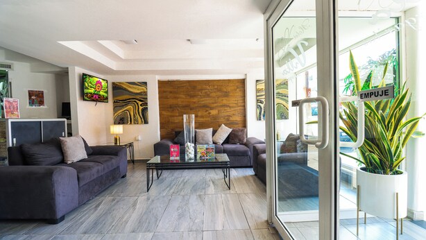 A modern living room with two sofas, a coffee table, and a TV. There is a wooden accent wall and a large window with a plant outside. - Hotel Villa Margaritas (Villahermosa)