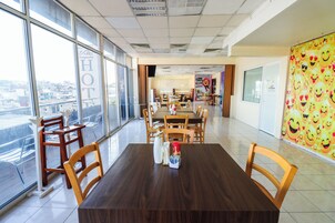 Uma sala de jantar de hotel com amplas janelas, mesas e cadeiras de madeira.