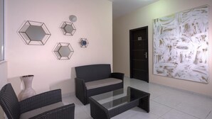 A modern living room with a sofa, two armchairs, a glass coffee table, and hexagonal mirrors on the wall. - Hotel Villa Margaritas (Villahermosa)