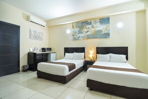 A hotel room with two beds, a desk, a small refrigerator, and a painting on the wall. - Hotel Villa Margaritas (Villahermosa)