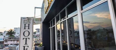 Un hotel con un letrero llamativo, mesas al aire libre y vistas de la ciudad.