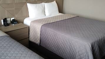 Una habitación de hotel con dos camas, un cabecero de madera, una mesita de noche con una lámpara y un mueble auxiliar con un teléfono y una cafetera.