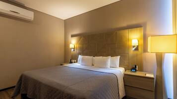 Een hotelkamer met een groot bed, twee nachtkastjes met lampen, een houten hoofdbord en een airconditioning aan de muur.