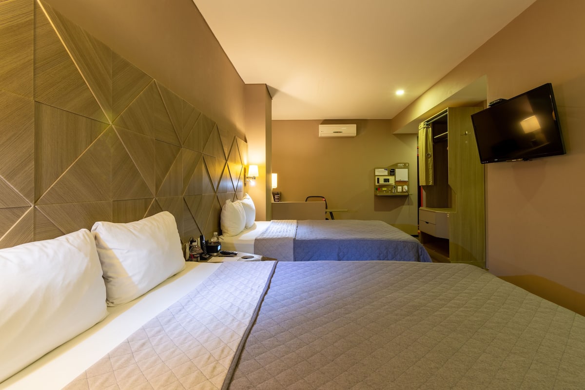 Una habitación de hotel con dos camas, televisión, espejo y armario.