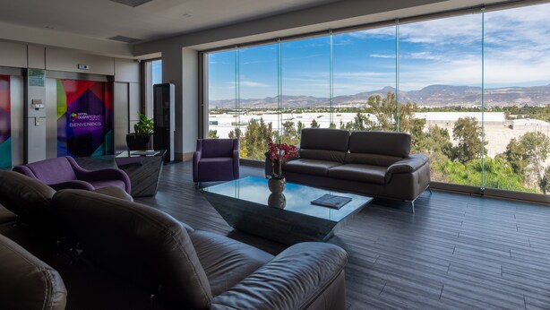 A modern hotel lobby with leather sofas, a glass coffee table, and a large window offering a view of the city and mountains. - Hotel Glow Point - Mulza (León)