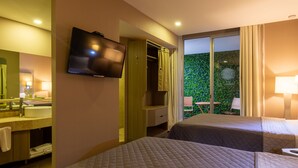 A hotel room with a bed, a television, a bathroom with a sink and mirror, and a view of greenery outside. - Hotel Glow Point - Mulza (León)