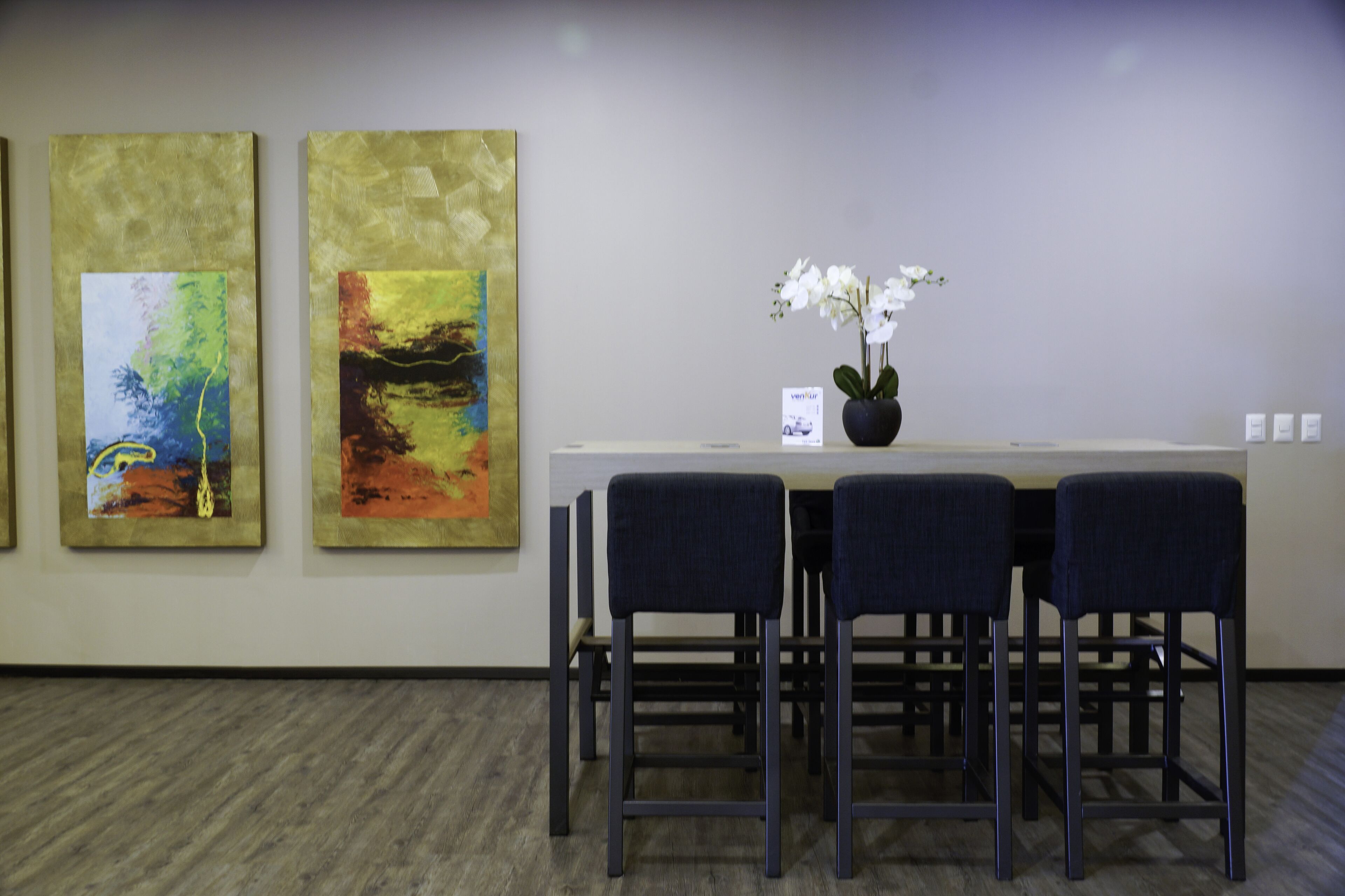 Zona de recepción con mostrador, dos sillones y dos grandes cuadros abstractos en la pared.
