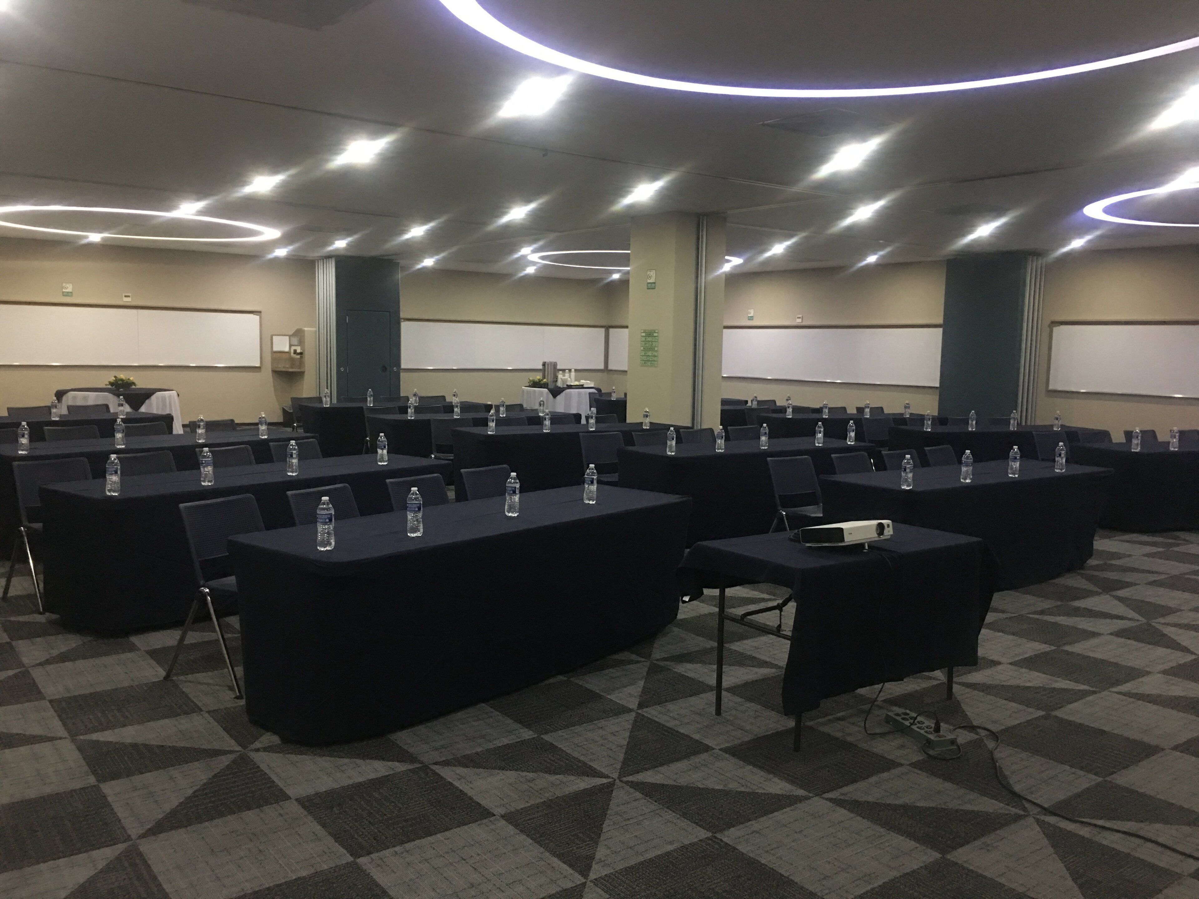 Un salón de conferencias con varias mesas, cada una con botellas de agua y un proyector.