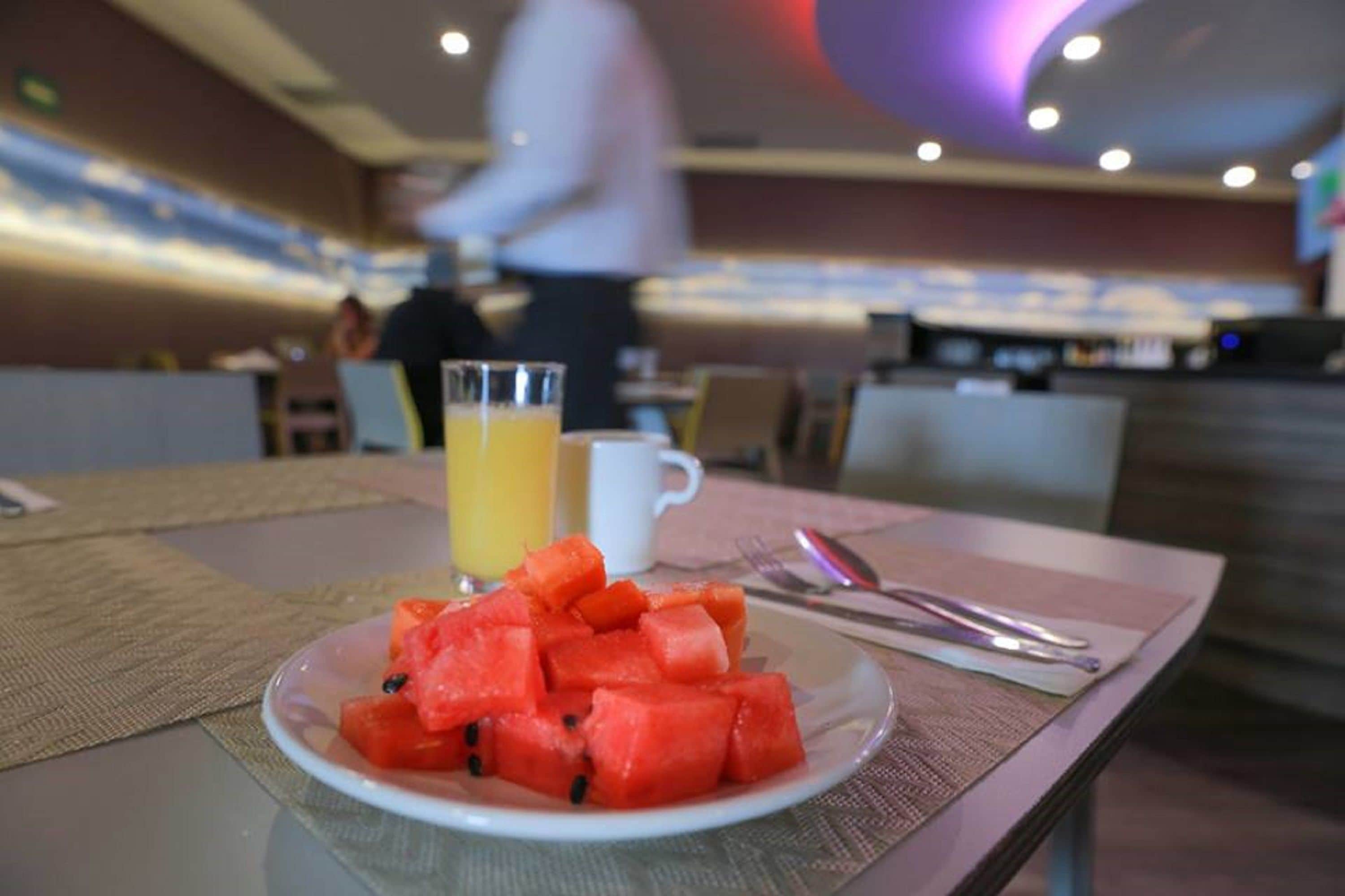 A breakfast setting with a plate of watermelon, a glass of orange juice, and cutlery on a table.