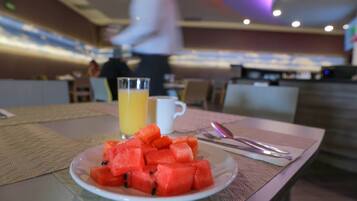 A breakfast setting with a plate of watermelon, a glass of orange juice, and cutlery on a table.