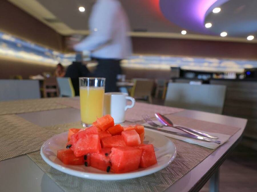 A breakfast setting with a plate of watermelon, a glass of orange juice, and cutlery on a table.