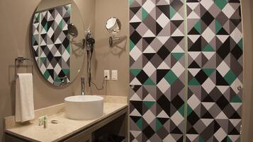Un baño moderno con un espejo redondo, un lavamanos y una ducha con puerta de diseño geométrico.