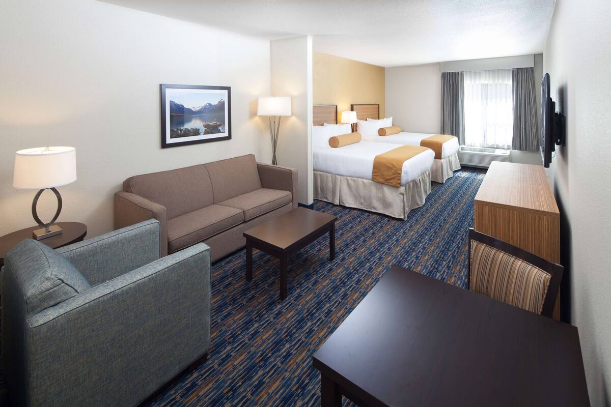 A hotel room with a sofa, a small table, a bed with two pillows, a TV, and a window with curtains.