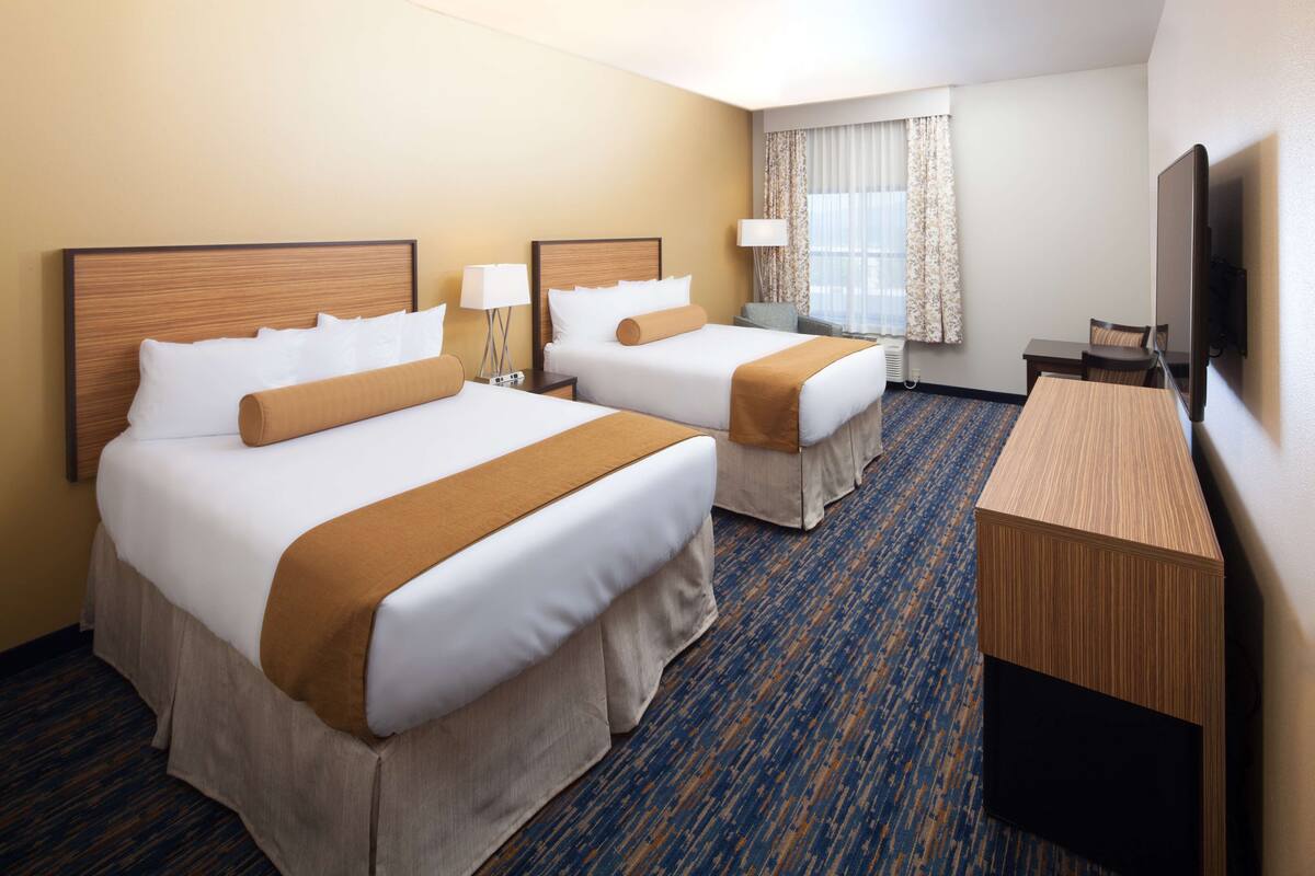 A hotel room with two beds, a desk, a TV, and a window with curtains.