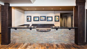 A reception area with a stone counter, framed artwork on the wall, and wooden pillars. - Red Lion Inn & Suites Polson (Polson)
