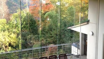 A balcony with a view of autumn foliage, wicker chairs, and potted plants.