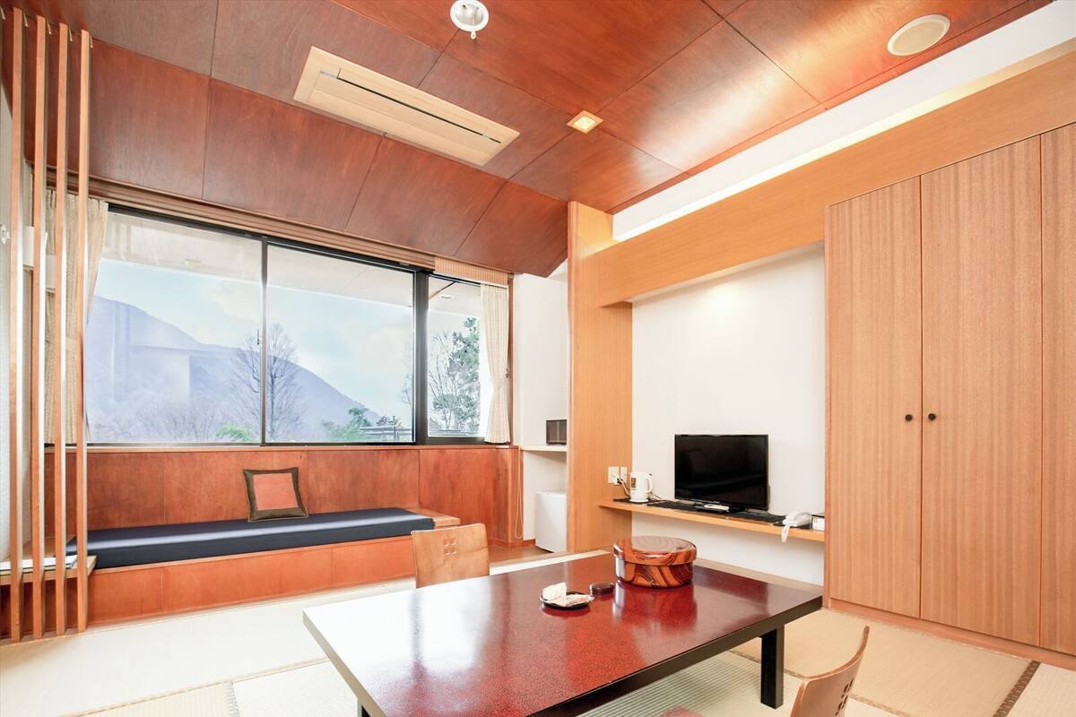 Ein modernes Zimmer mit Holzbalkendecke, einem großen Fenster, einer Couch, einem Fernseher und einem Tisch.
