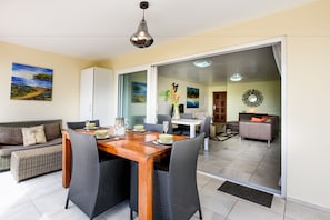 A dining area with a wooden table and wicker chairs, a sofa, and a painting on the wall. - Ocean Apartments (Willemstad)