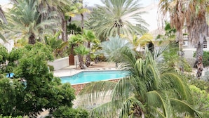 A pool surrounded by palm trees and lush greenery, with a building in the background. - Ocean Apartments (Willemstad)