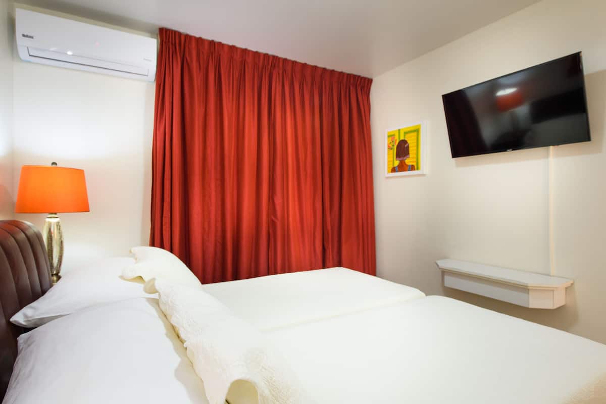 A hotel room with a bed, a TV, a red curtain, and a wall-mounted air conditioner.