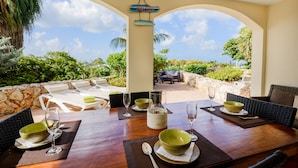 An outdoor dining area with a stone wall, wicker furniture, and a view of the garden. - Ocean Apartments (Willemstad)