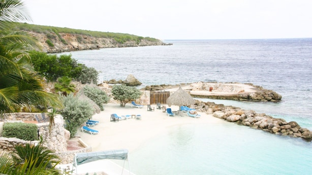 A beach with clear turquoise water, a stone wall, and a few lounge chairs. - Ocean Apartments (Willemstad)
