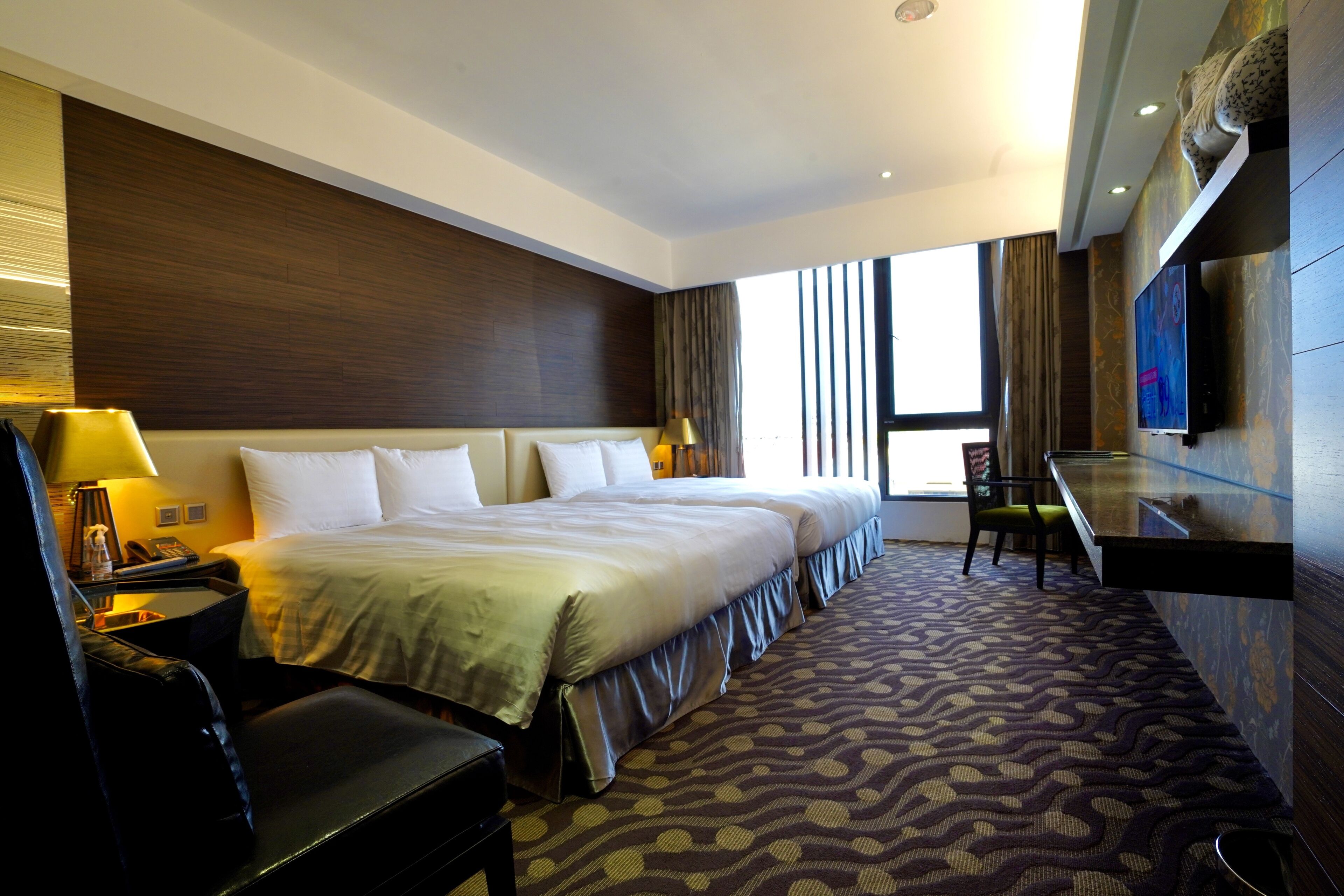 A hotel room with a large bed, a desk, a chair, a TV, and a window with curtains.