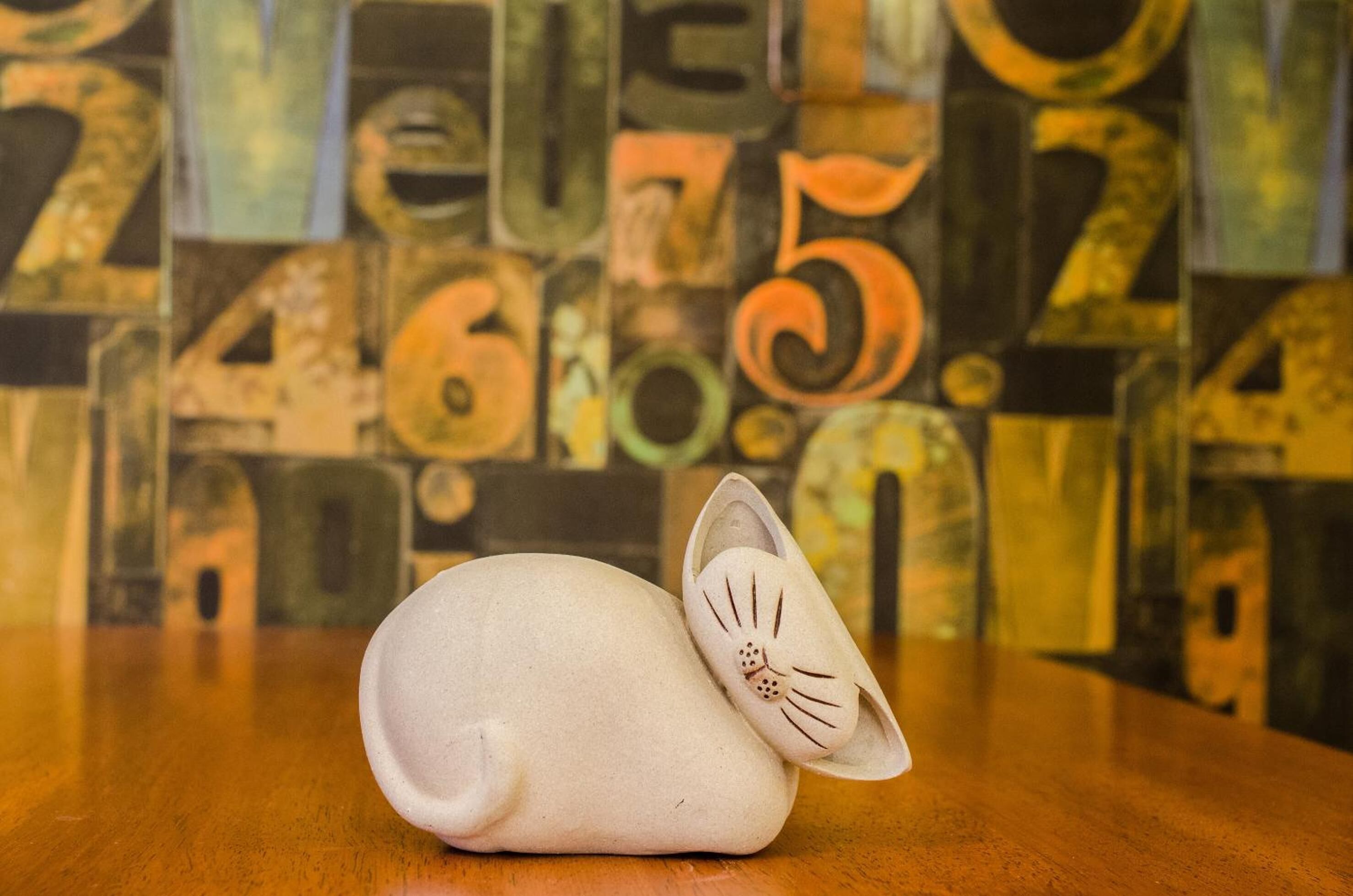 A ceramic cat figurine on a wooden table with a background of abstract numbers and letters.