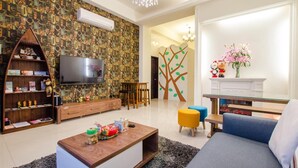 A living room with a television, wooden furniture, a tree mural, and a glass coffee table. - Smokey Cat B&B (Taitung)