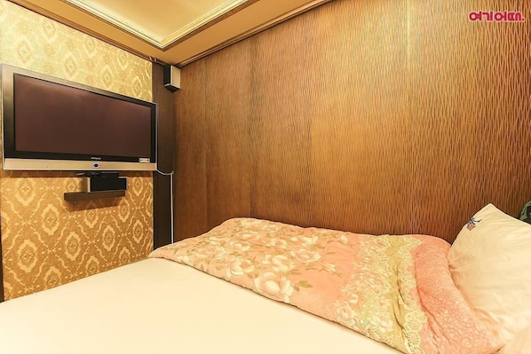 Habitación de hotel con cabecera de madera, un televisor de pantalla plana montado en la pared y una cama con ropa de cama estampada con motivos florales.